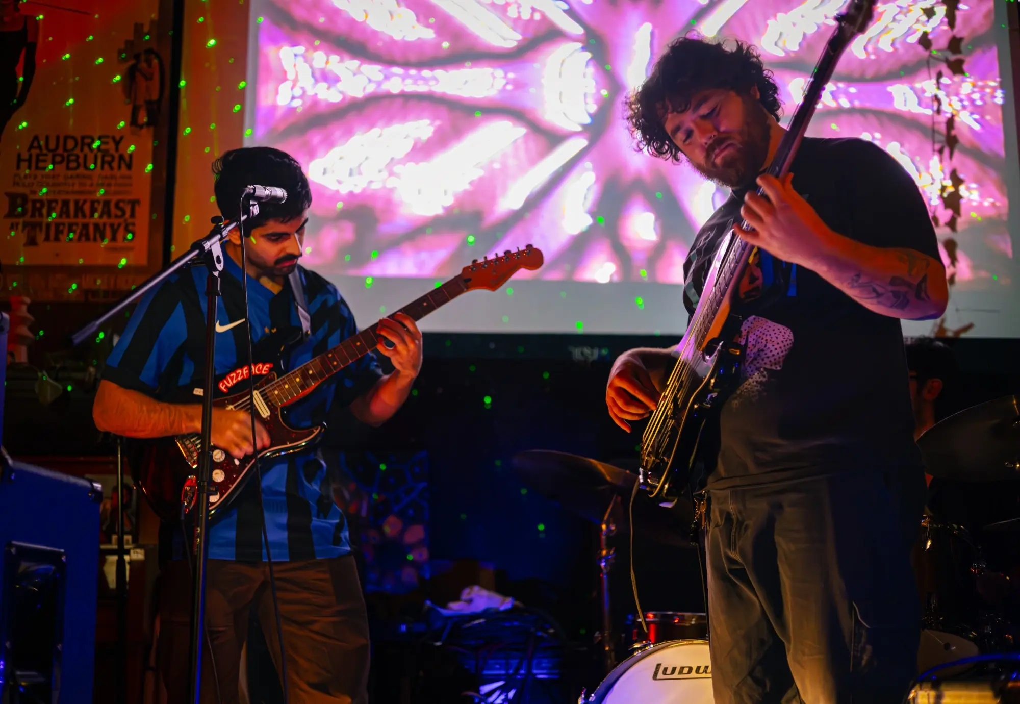 Two guitarists playing under a pink psychedelic projection