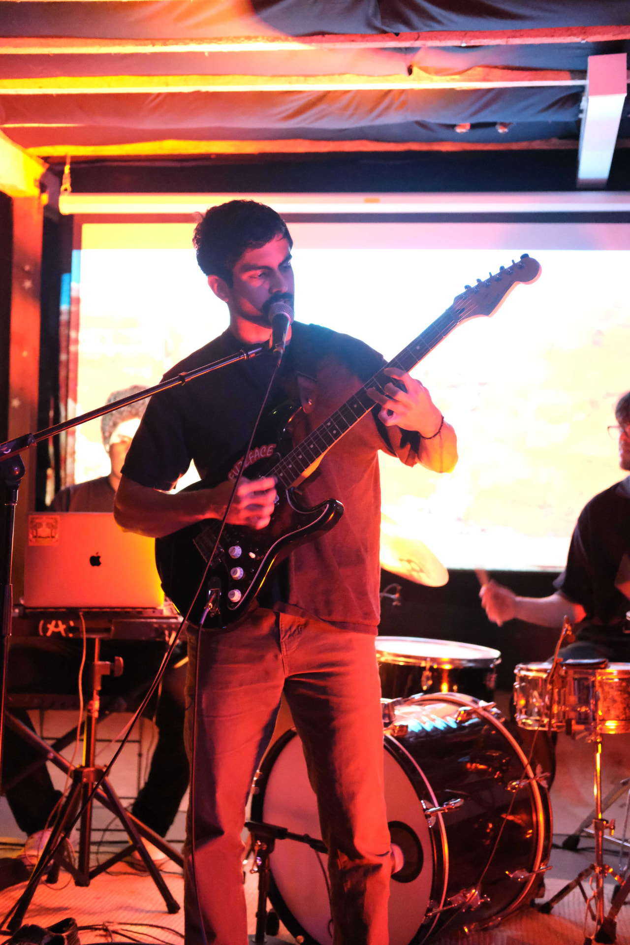 Singer playing guitar into a mic under warm red stage light